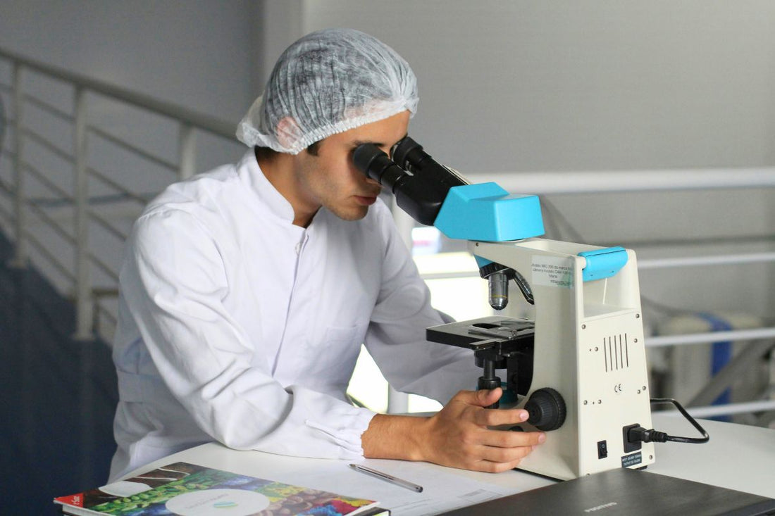 A man in a lab coat examines methylene blue through a microscope